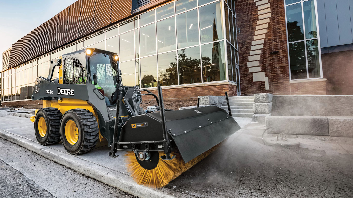 John Deere Skid Steer with Angle Broom attachment sweeping sidewalks in front of business